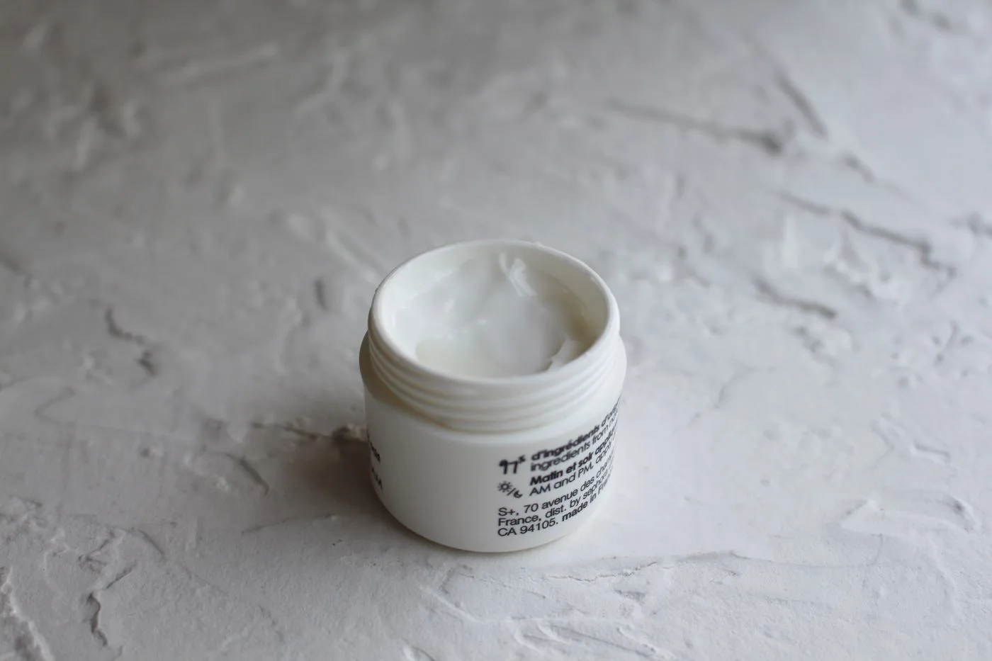 An open jar of face cream on a textured neutral surface